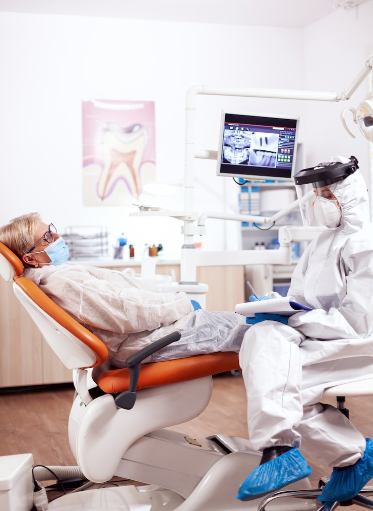 dentist-assistant-wearing-hazmat-suit-against-coronavirus-taking-notest-talking-with-senior-patient-elderly-woman-protective-uniform-medical-examination-dental-clinic_482257-12570